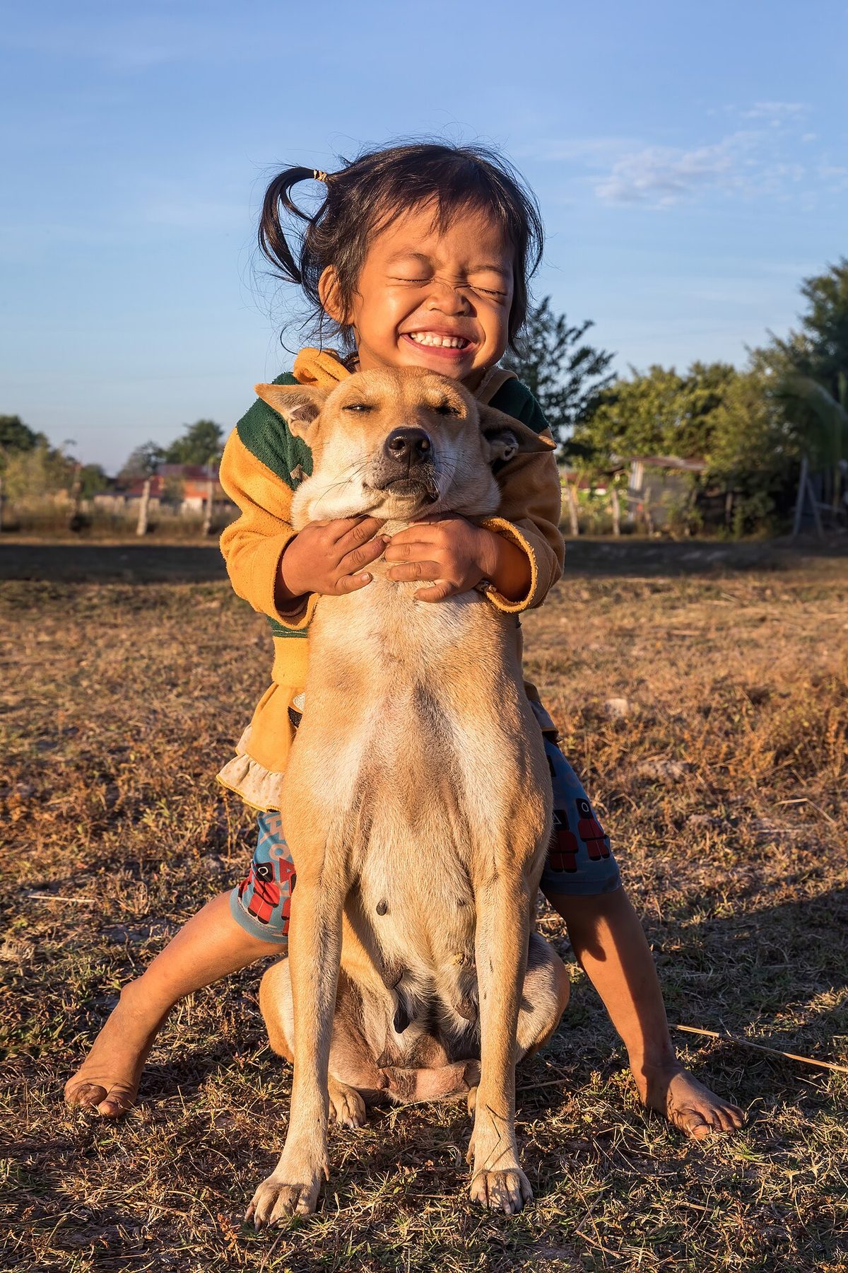 Human–canine friendship - girl hugging her dog tightly at golden hour in Laos