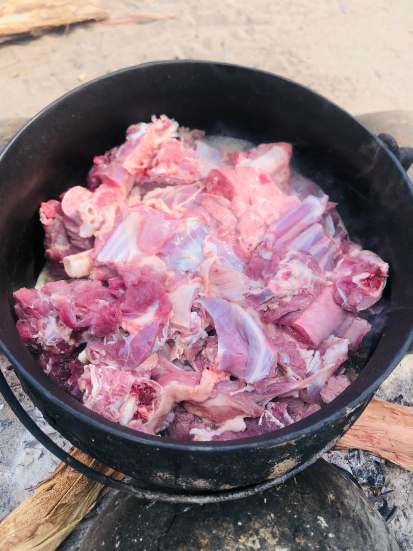 Fresh goat meat in a three legged potjie pot on fire